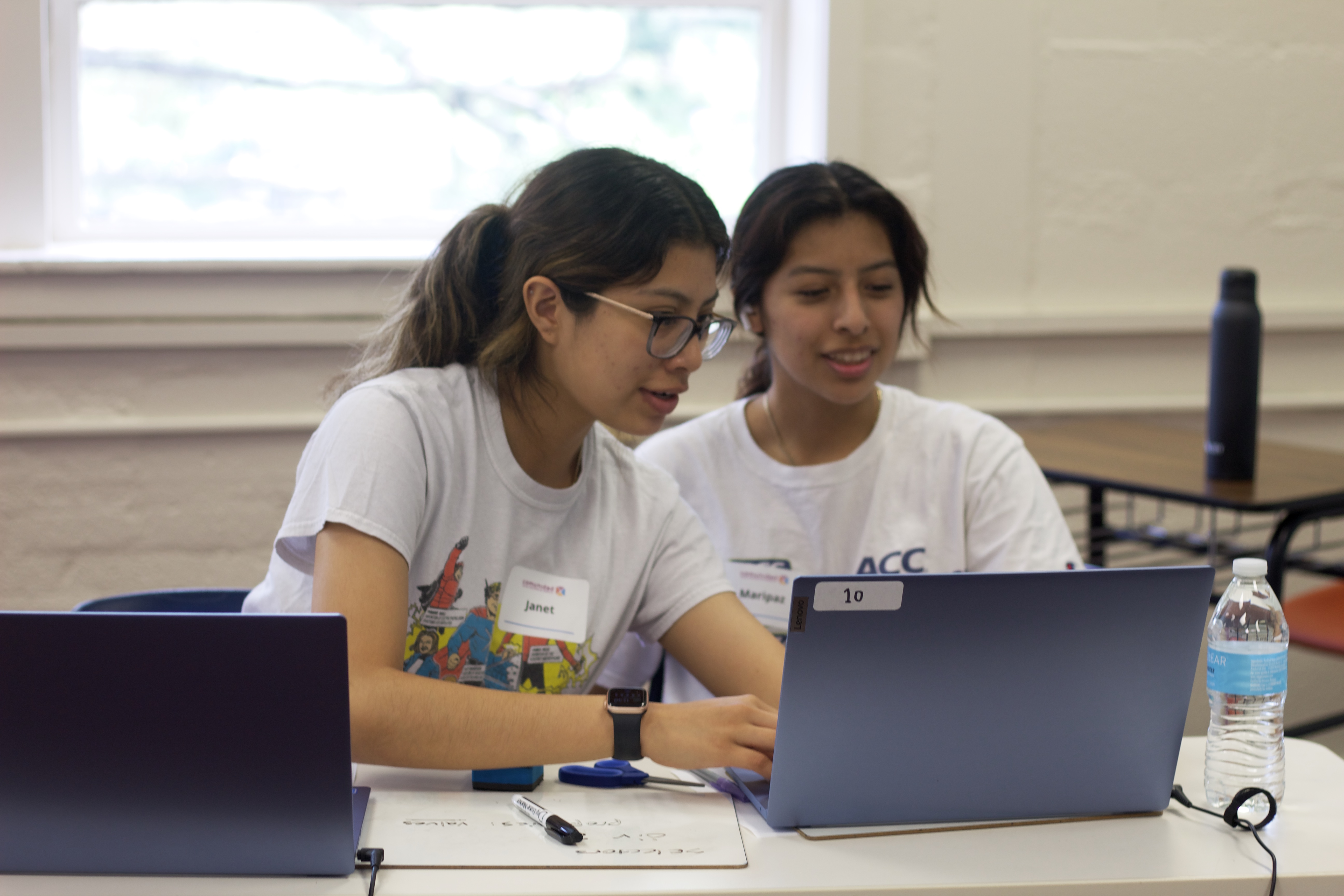 One student helps another by pointing to her screen