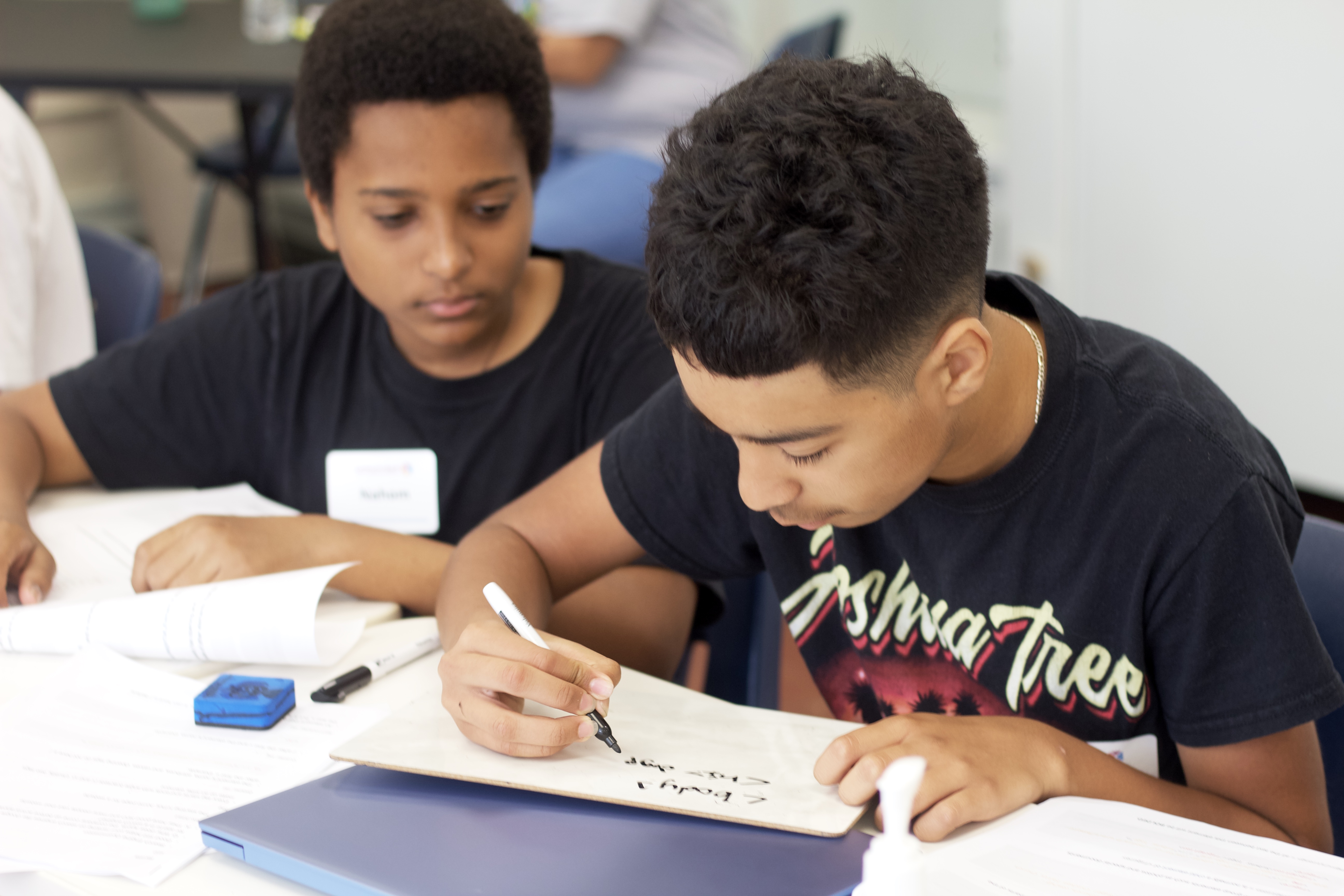 One students writes out HTML on a whiteboard while the other watches